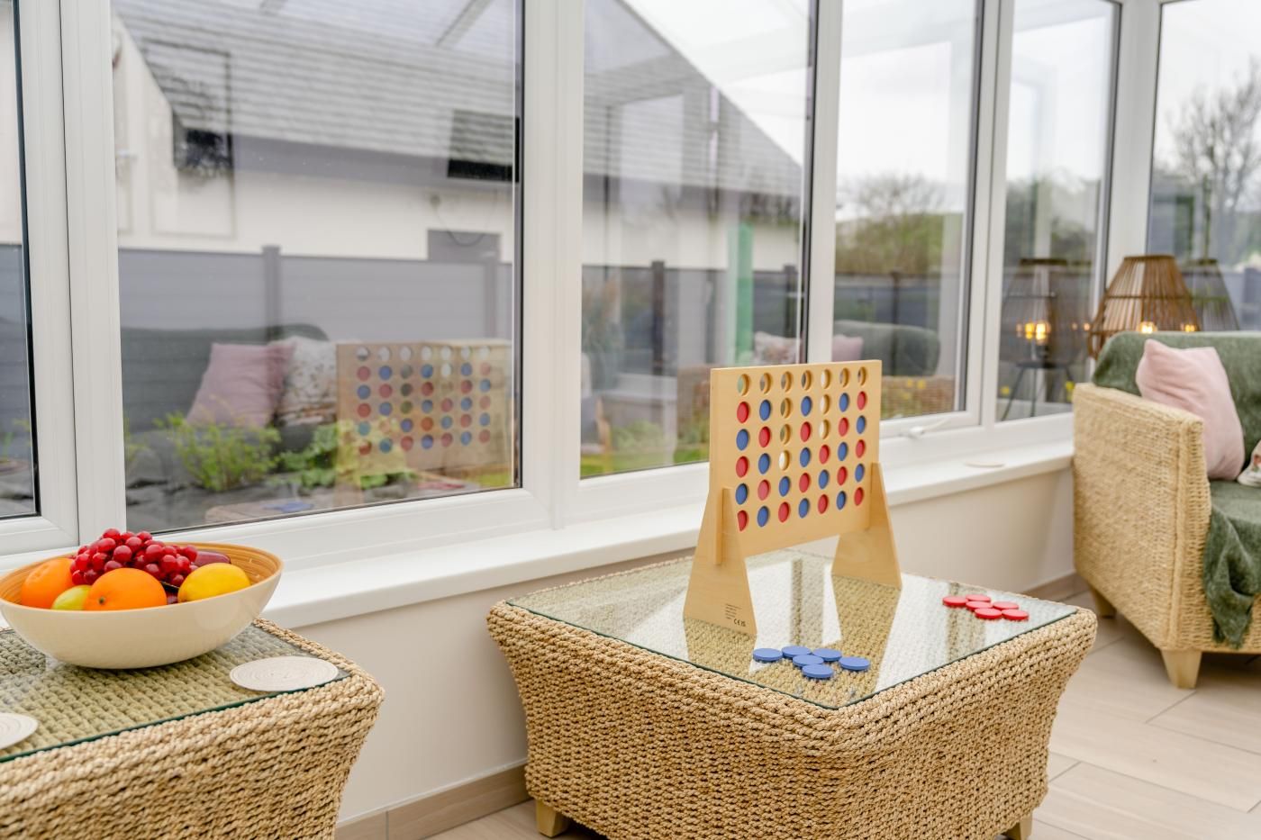 A room with a large window, wicker furniture, a bowl of fruit, and a pegboard game.