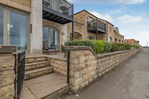 A stone building with a balcony, steps leading to the entrance, and a paved walkway. - 2 Bed in Seahouses (oc-p39046) (Seahouses)