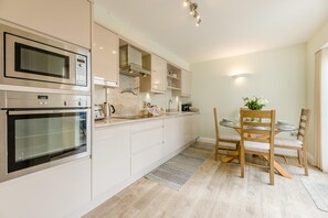 A modern kitchen with built-in appliances, a dining area with a table and chairs, and a light-colored floor. - 2 Bed in Seahouses (oc-p39046) (Seahouses)