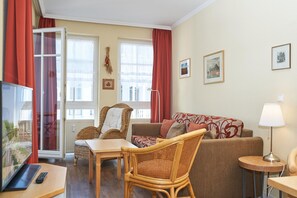 Ein Wohnzimmer mit einer Couch, Sesseln, einem Tisch, einem Fernseher und einer Lampe.