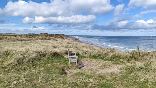 A beach with dunes, a wooden bench, and a signpost. - 2 Bed in Seahouses (oc-s34710) (Seahouses)