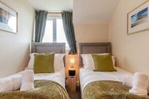 A twin room with two beds, a nightstand, a lamp, and a window with curtains. - 2 Bed in Seahouses (oc-s34710) (Seahouses)