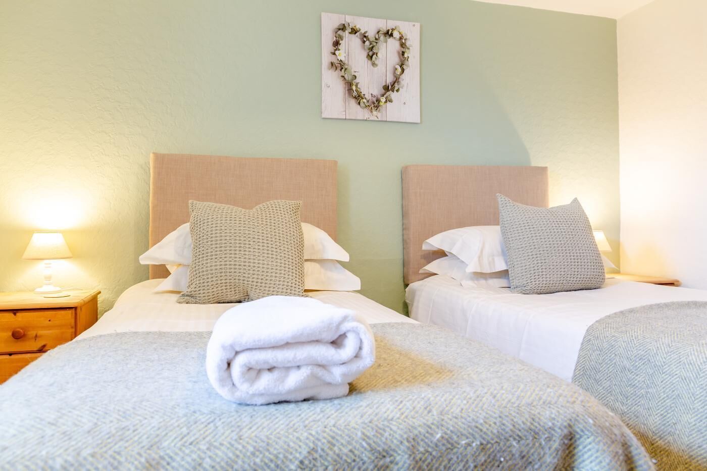 Habitación de hotel con dos camas, una mesita de noche con lámpara y una decoración con forma de corazón en la pared.