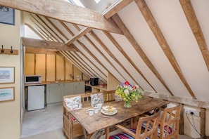 A rustic kitchen with wooden beams, a dining table with floral tableware, and a view of the adjacent living area.