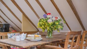 A dining table with a floral arrangement, plates of food, and a kettle in a room with wooden beams.