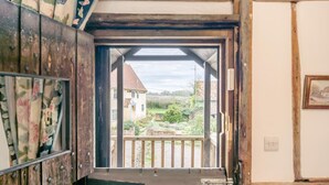 A wooden staircase leading to a balcony with a view of a house and garden.