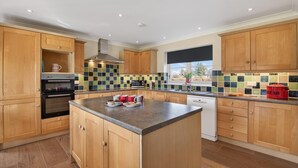 A modern kitchen with wooden cabinets, a central island, a built-in oven, and a window with a view. - 5 Bed in Cockburnspath (oc-r35051) (Cockburnspath)