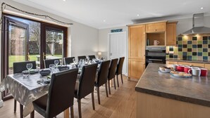 A modern kitchen with wooden cabinets, a dining area with a table set for six, and a view of the outdoors. - 5 Bed in Cockburnspath (oc-r35051) (Cockburnspath)
