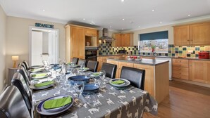A dining area with a table set for six, kitchen cabinets, a microwave, and a tiled backsplash. - 5 Bed in Cockburnspath (oc-r35051) (Cockburnspath)