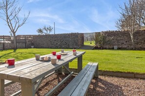 A picnic table with cups and food, set against a stone wall and grassy area. - 5 Bed in Cockburnspath (oc-r35051) (Cockburnspath)