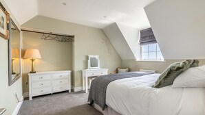 Une chambre avec un plafond en pente, un lit avec une literie blanche, une commode, un miroir et une fenêtre.