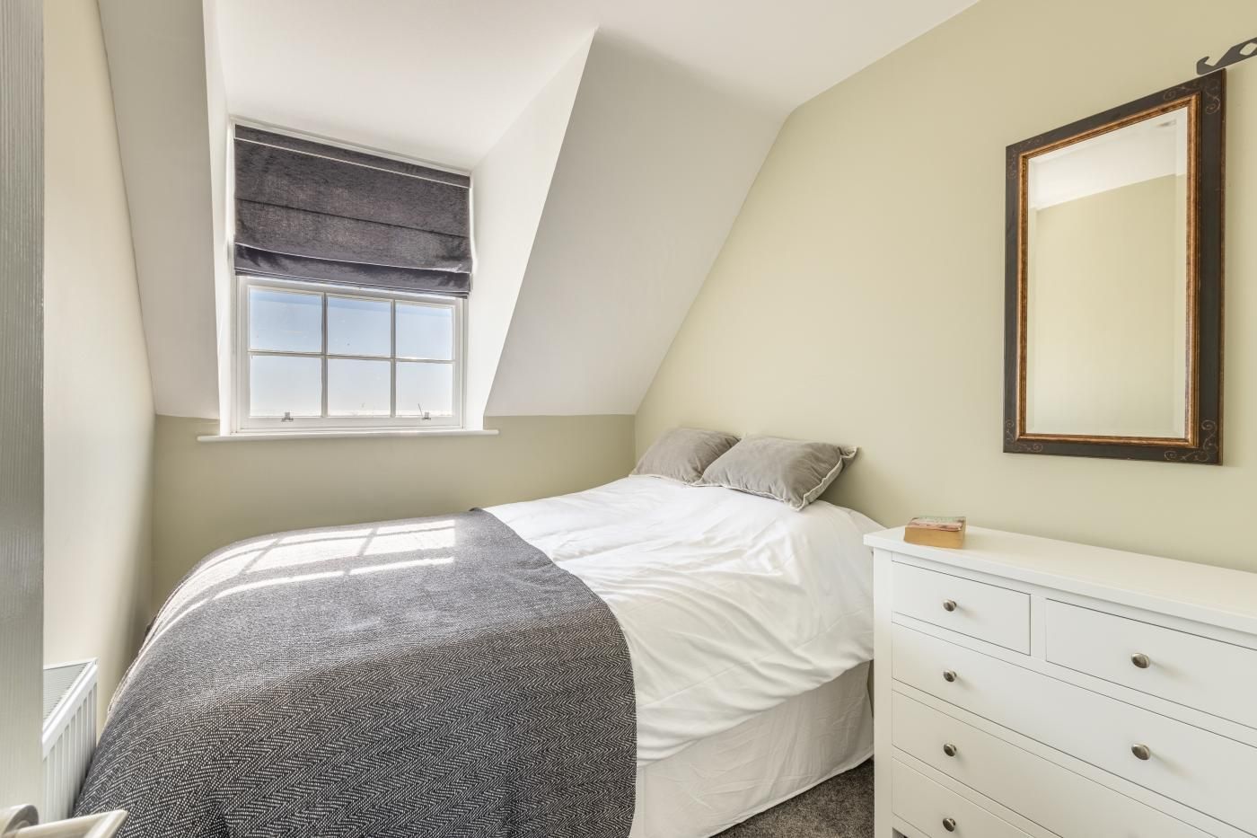 A bedroom with a bed, a dresser, a window with a blind, and a mirror on the wall.