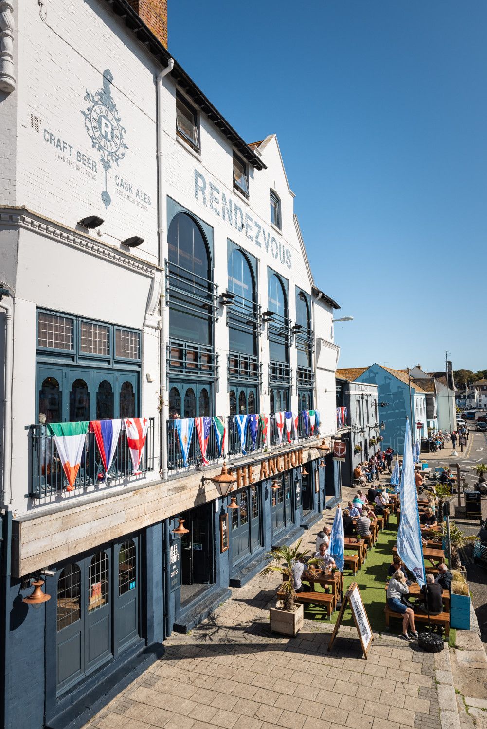A building with a sign 'Rendezvous' and a row of flags on the balcony.
