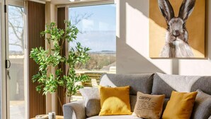 Ein graues Sofa mit zwei senffarbenen Kissen, ein Holznachttisch, ein Topfpflanze und ein gerahmtes Bild von einem Hasen an der Wand.