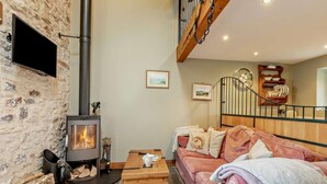 Una sala de estar acogedora con una pared de piedra, una chimenea, un sofá, una mesa de centro de madera y una escalera.