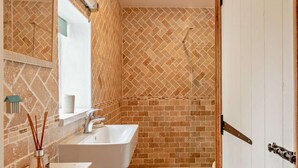 Un baño con un lavabo blanco, un espejo y una zona de ducha con un patrón de baldosas en espiga.