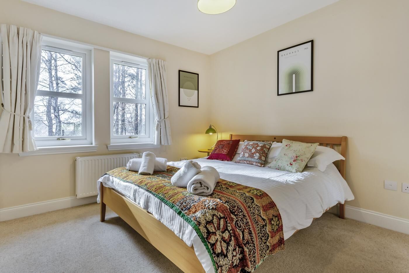 Une chambre à coucher avec un lit, deux fenêtres, un radiateur, une lampe et un tableau encadré au mur.