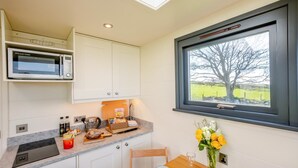 Cozinha com micro-ondas, armários, pia e janela com vista para uma árvore e um campo.