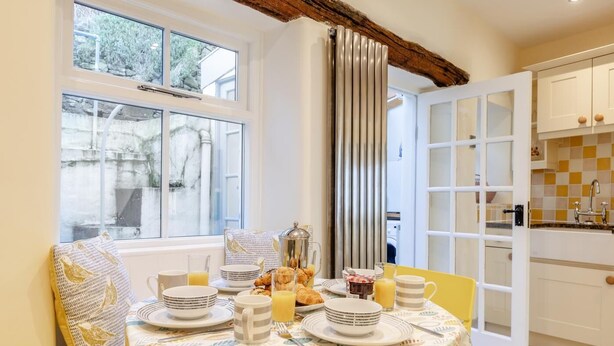 A dining area with a table set for breakfast, a window with a view, and a kitchen area visible through an open door. - 3 Bed in Tideswell (oc-w39004) (Tideswell)