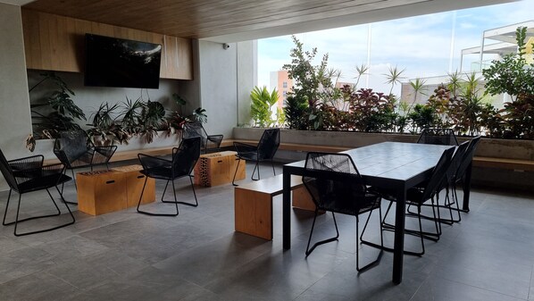 A modern dining area with a large table and chairs, surrounded by potted plants and a city view.