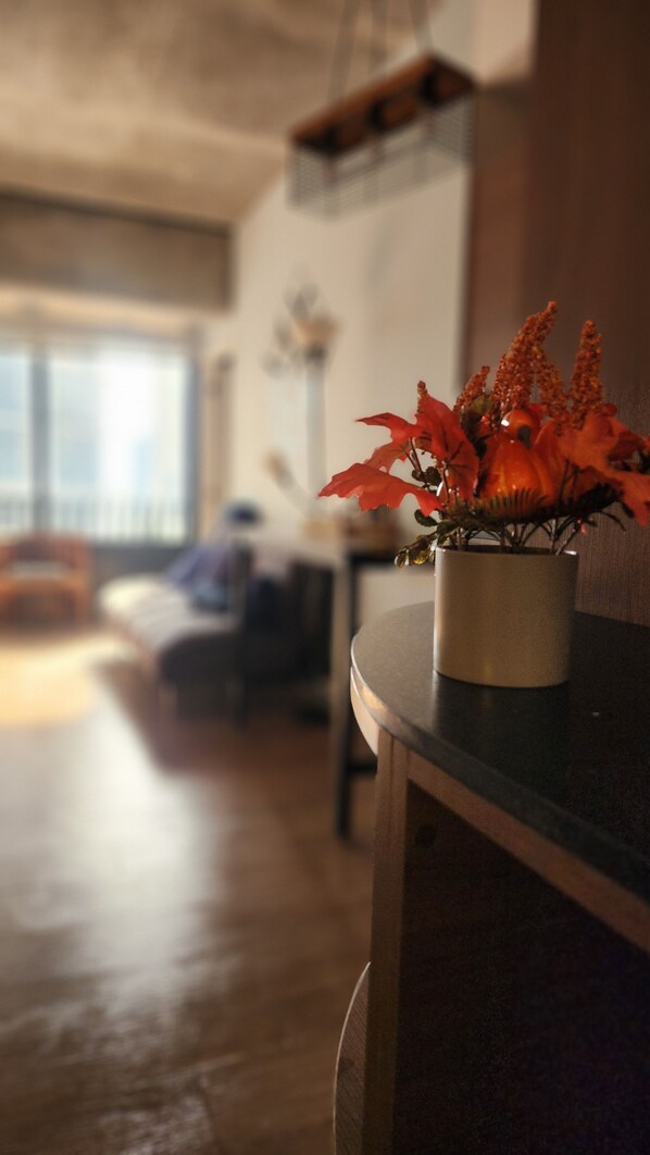 A room with a wooden floor, a potted plant on a table, and a window with blinds.