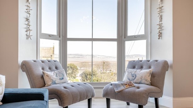 Ein Zimmer mit zwei grauen Polstersesseln, einem blauen Sofa und einem großen Fenster mit Landschaftsblick.