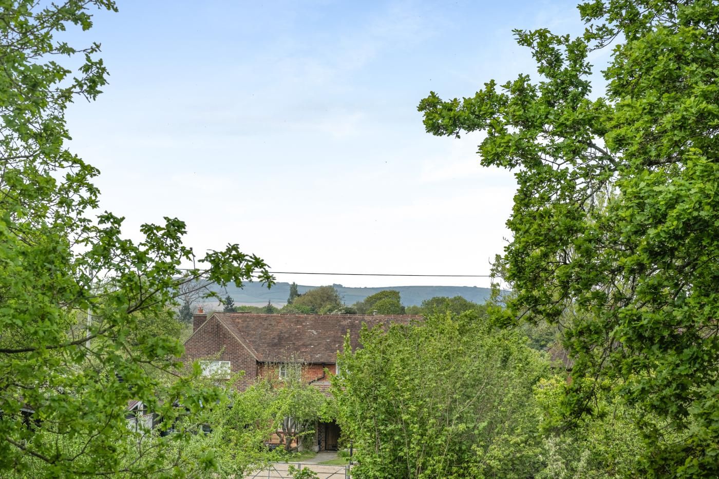 Une maison de campagne aux murs en briques, entourée d’une végétation luxuriante et d’arbres.
