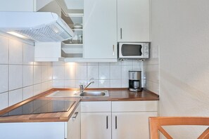 Eine Küche mit weißen Schränken, einer Mikrowelle, einer Kaffeemaschine und einem Edelstahlspülbecken.