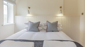 Een hotelkamer met een groot bed, twee bedlampjes, een raam en een wit hoofdeinde.