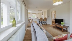 Een moderne woonkamer met een bank, een televisie en een eethoek op de achtergrond.