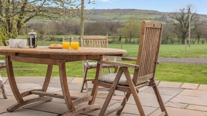 Een houten tuintafel met stoelen, een koffiepot en glazen jus d'orange.