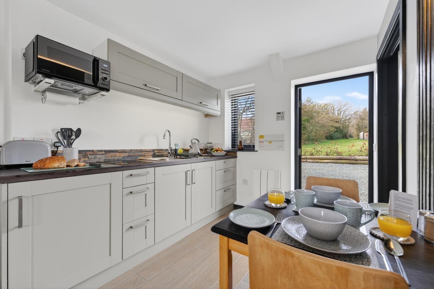 Una cocina moderna con armarios blancos, microondas integrado y una zona de comedor con mesa puesta para dos.