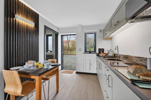 Eine moderne Küche mit Essbereich, ausgestattet mit einem Holztisch, Stühlen und Blick ins Freie.