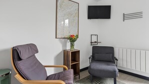 A modern living room with a wooden chair, a grey armchair, a flat-screen TV, a wall-mounted shelf, and a radiator. - 1 Bed in Minsterley (oc-s38642) (Minsterley)