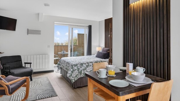 A modern hotel room with a bed, a dining table set for breakfast, a TV mounted on the wall, and a sliding glass door leading to an outdoor area. - 1 Bed in Minsterley (oc-s38642) (Minsterley)