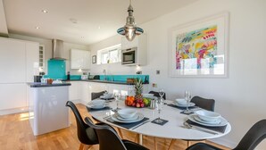 Una cocina moderna con armarios blancos, una isla central y un comedor con una mesa redonda para cuatro.