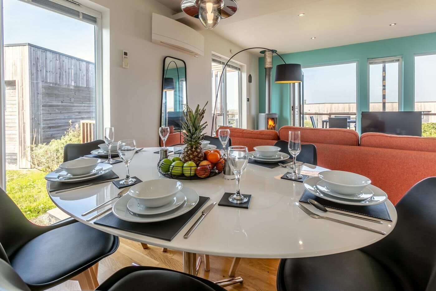 A dining area with a round table set for six, surrounded by black chairs, a fruit bowl, and a fireplace.