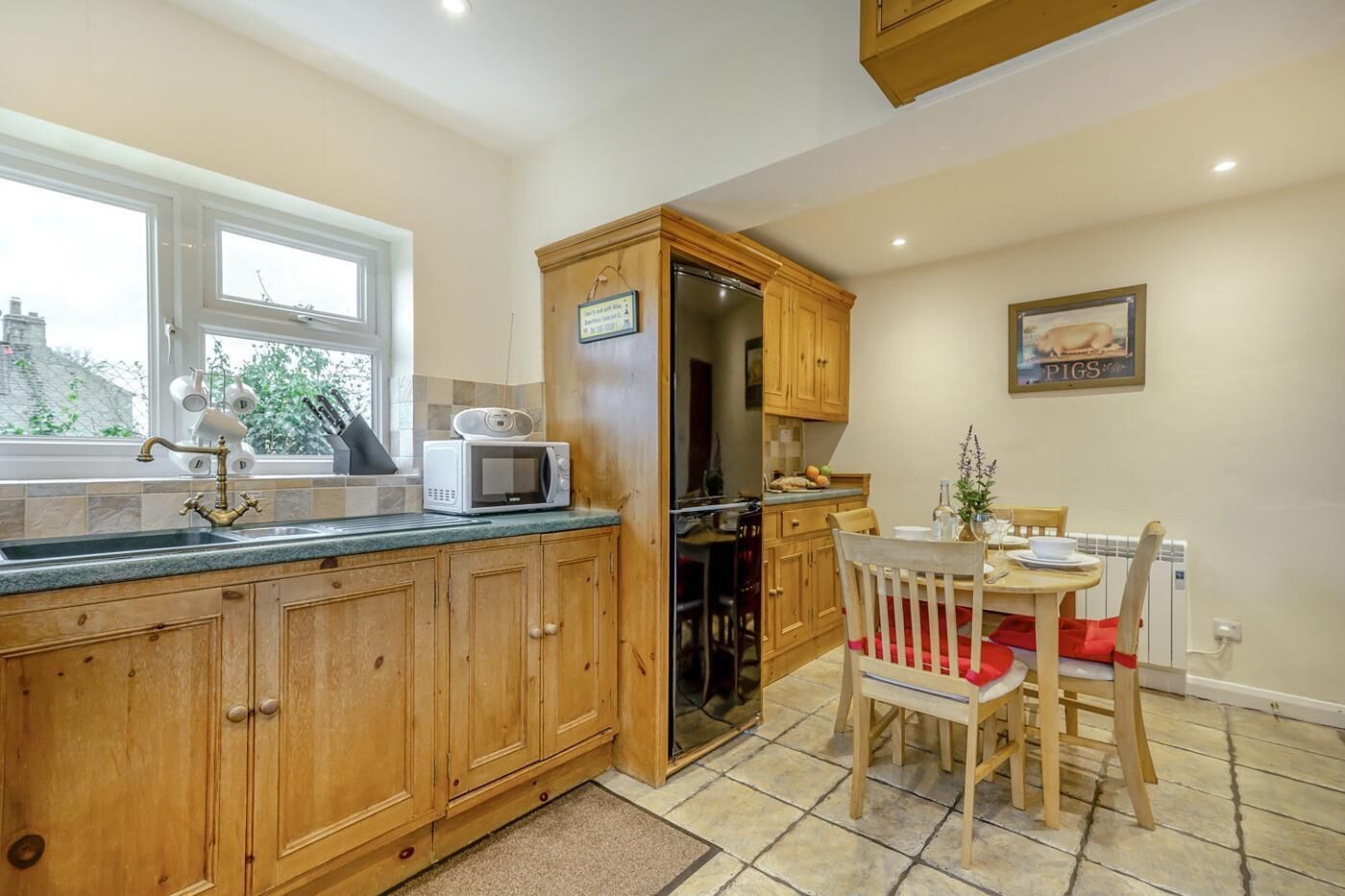 Una cocina con armarios de madera, microondas, lavabo y comedor con mesa y sillas.