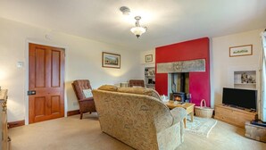 Una sala de estar con sofá, sillón, chimenea, televisión, estantería y una puerta.