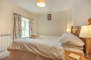 Een hotelkamer met een bed, een bedlamp, een radiator en een raam met gordijnen.