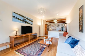 Ein Wohnzimmer mit Fernseher, Holzmöbeln, einem gemusterten Teppich und einer Treppe, die zur Küche führt.