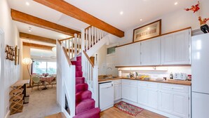 Una cocina con armarios blancos, una escalera de madera y una zona de comedor con una mesa y sillas.