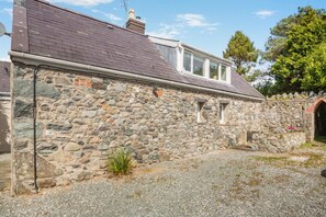A stone building with a sloped roof, a small window, and a gravel driveway. - 1 Bed in Llandwrog (oc-h36065) (Llandwrog)