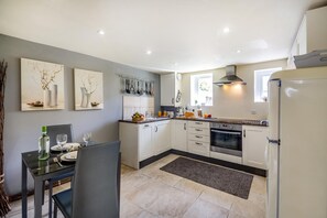 A modern kitchen with white cabinets, a stainless steel oven, and a dining area with a table and chairs. - 1 Bed in Llandwrog (oc-h36065) (Llandwrog)