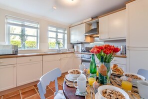 Una cocina moderna con armarios blancos, encimera de madera y una mesa de comedor preparada para el desayuno.