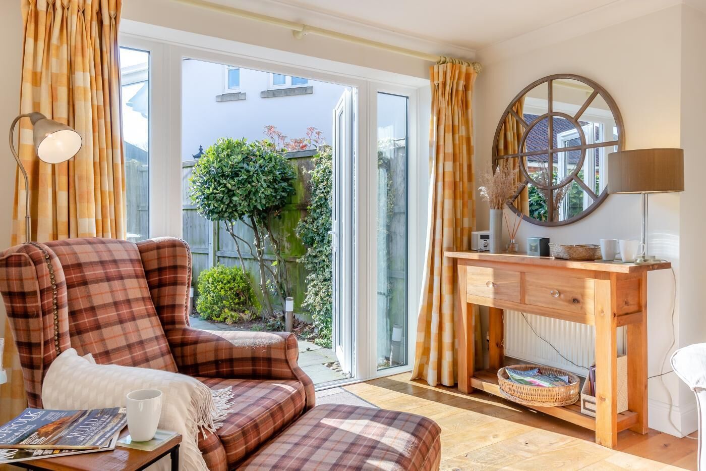 A cozy living room with a plaid sofa, a wooden desk, and a large window with curtains.