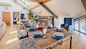 A modern dining area with a wooden table set for six, a hanging light fixture, and a view of the kitchen in the background. - 2 Bed in Borth (oc-ystiw4) (Glanwern)