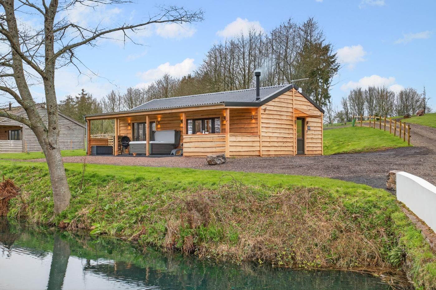 Une cabane en rondins avec une véranda, un barbecue et une vue sur un plan d’eau.