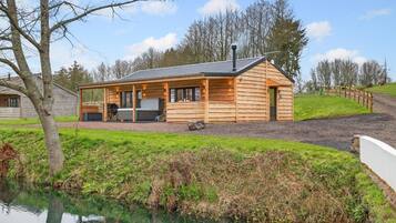 Une cabane en rondins avec une véranda, un barbecue et une vue sur un plan d’eau.