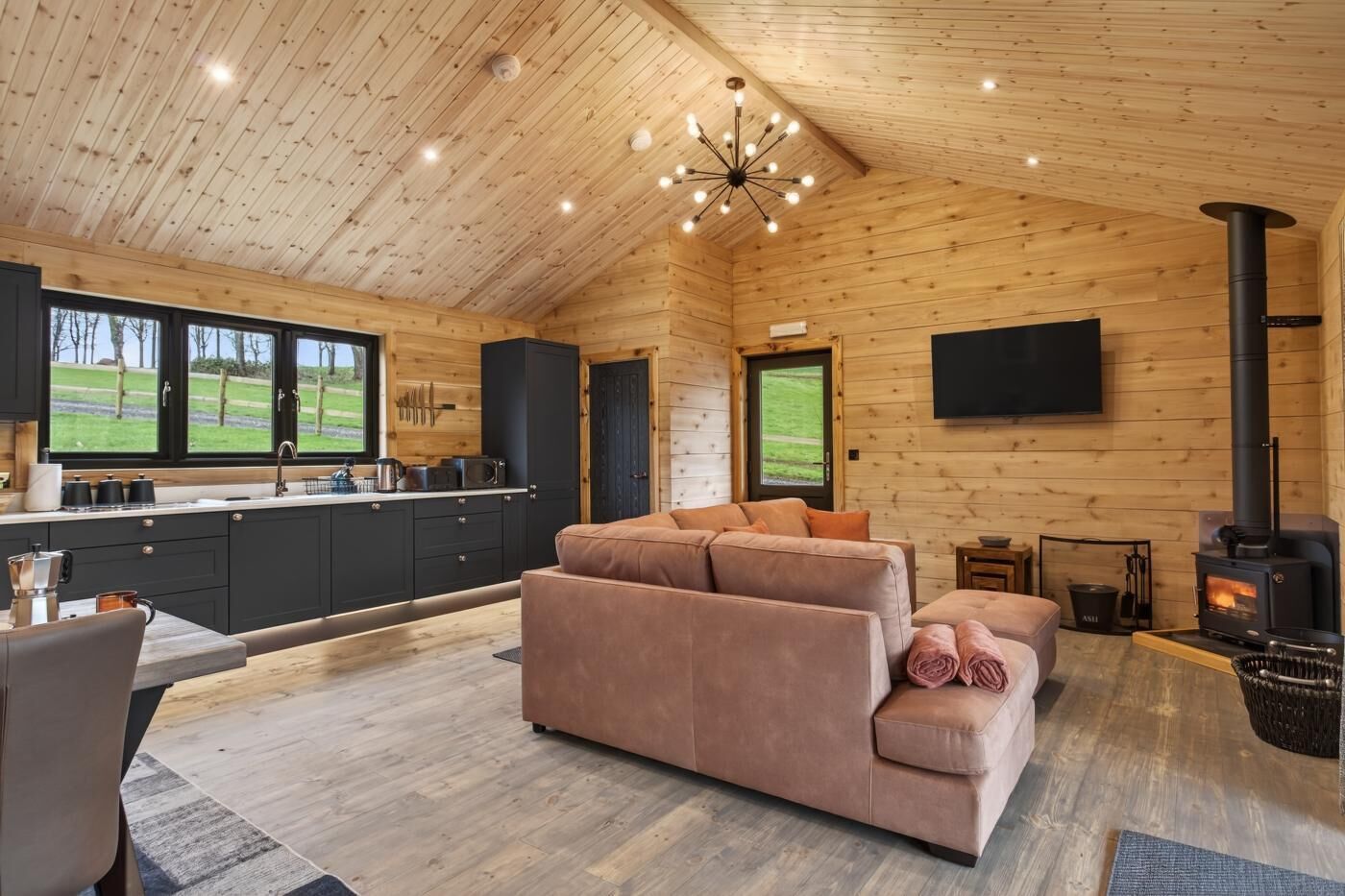 L'intérieur d'une cabane en rondins comprend une cuisine, un canapé, une cheminée et de grandes fenêtres.